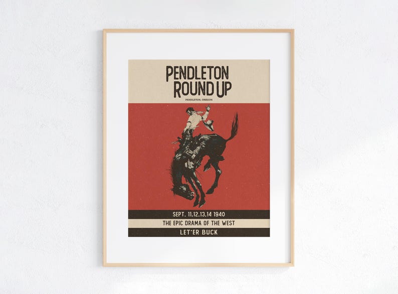 May include: Framed vintage poster for the Pendleton Round Up rodeo event. The poster features a cowboy riding a bucking bronco, with text including "Pendleton Round Up" and "Sept. 11,12,13,14 1940". The colour scheme is red, beige, and black.