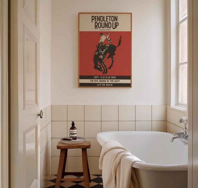 May include: A framed vintage poster with the text "PENDLETON ROUND UP" and a rodeo scene graphic hangs above a white bathtub. The poster has a red background and is in a bathroom setting with a wooden stool and a bottle.