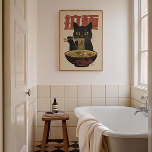 May include: A black cat with a bowl of noodles in front of it. The cat is looking at the camera and has a playful expression. The bowl of noodles is in a white bowl with a red rim. The image is in a wooden frame and has the Japanese characters "猫麺" written on it.
