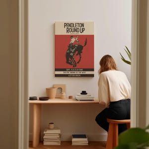 May include: A framed poster with the text "PENDLETON ROUND UP" and an illustration of a rodeo rider on a bucking bronco. The poster has a red background with black text and a cream-colored top section. The text reads "SEPT. 11,12,13,14 1940 THE EPIC DRAMA OF THE WEST LET'ER BUCK."