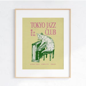 May include: Framed art print featuring a cat playing a piano. The print has the words "TOKYO JAZZ CLUB" in pink, with Japanese text above the cat illustration. The cat is white with gray markings, and the piano is green.