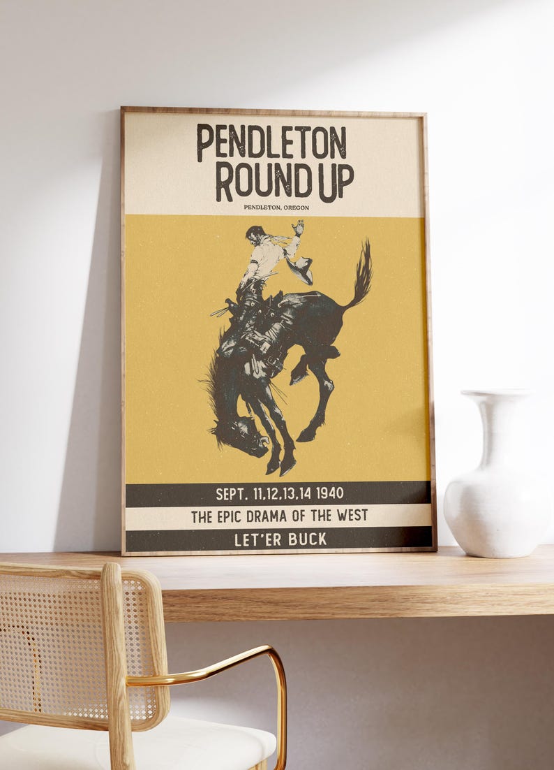 May include: Framed vintage poster for the Pendleton Round Up rodeo event. The poster features a black and white illustration of a cowboy riding a bucking bronco against a yellow background. Text includes event details.
