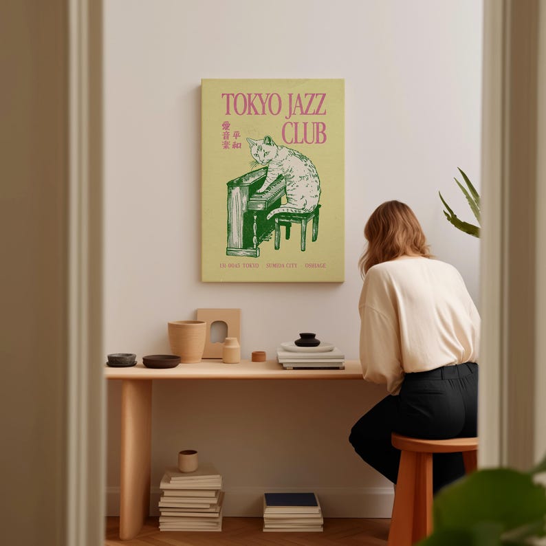 May include: A framed poster with the text "TOKYO JAZZ CLUB" in pink and green, featuring a cat playing a piano. The poster is displayed on a white wall above a wooden desk with various decorative items.