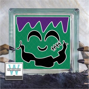 May include: Green glass block with a black and white Frankenstein face design. The face has a stitched scar and a purple top.