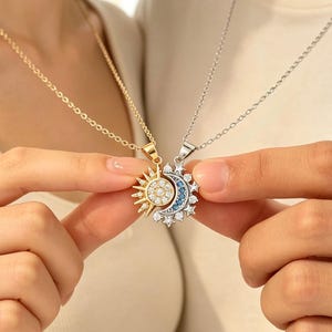 May include: A gold-toned sun pendant necklace with clear crystals and a silver-toned crescent moon pendant necklace featuring blue and clear crystals. The two pendants are designed to interlock, creating a cohesive celestial-themed jewelry set.