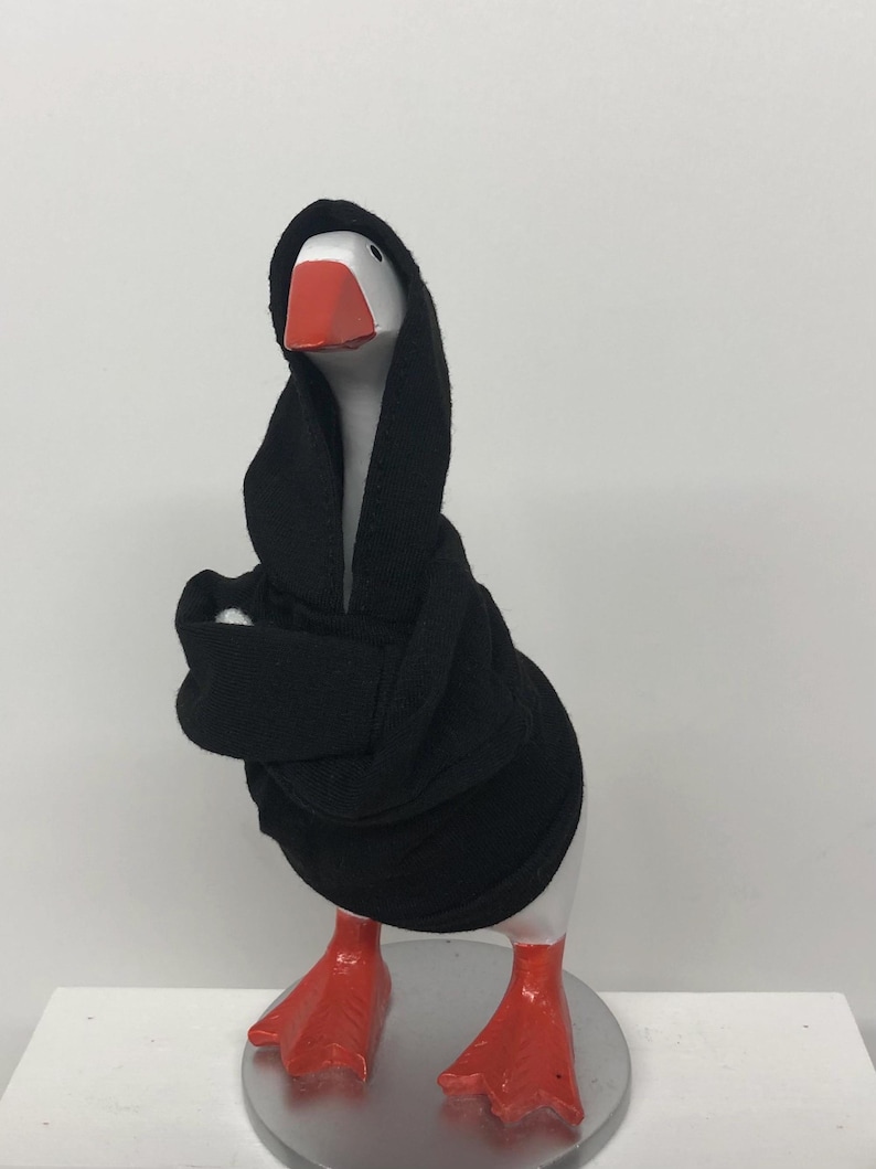 May include: A whimsical goose figurine with a white body, a red beak and feet, and a black hooded robe. The figurine is standing on a silver base. The goose is a unique decorative item.