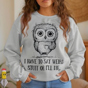 Peut inclure: Un sweat-shirt gris clair avec une illustration en noir et blanc d'un hibou tenant une tasse à café. Le texte "I HAVE TO SAY WEIRD STUFF OR I'LL DIE" est imprimé en dessous. Le sweat-shirt a des manches longues et un col rond.