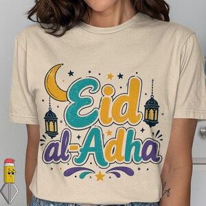Może przedstawiać: Beżowa koszulka z kolorowym wzorem "Eid al-Adha". Projekt zawiera żółty półksiężyc, gwiazdy, lampiony i tekst w kolorze turkusowym, żółtym i fioletowym. Koszulka ma okrągły dekolt i krótkie rękawy.