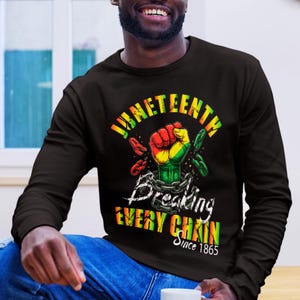 Peut inclure: T-shirt noir à manches longues avec un motif célébrant le Juneteenth. Le design présente un poing fermé rouge, jaune et vert, brisant des chaînes. Le texte comprend "Juneteenth", "Breaking Every Chain" et "Since 1865".