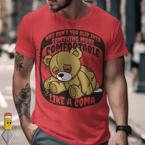 May include: Red t-shirt with a graphic of a yellow teddy bear with a sad expression. The text on the shirt reads "WHY DON'T YOU SLIP INTO SOMETHING MORE COMFORTABLE LIKE A COMA".