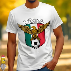 Peut inclure: T-shirt blanc avec un motif d'aigle doré aux ailes déployées, perché sur un ballon de football. Le design comprend le mot "MÉXICO" au-dessus de l'aigle, sur un écusson aux rayures vertes, blanches et rouges.