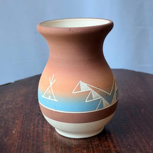 May include: A small ceramic vase with a flared rim and a rounded body. The exterior features a gradient of terracotta, orange, and blue, decorated with white etched geometric patterns including a teepee and mountain shapes, with a cream base.