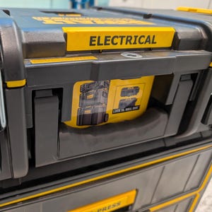 May include: Black and yellow electrical tool storage box with the word "ELECTRICAL" in yellow. The box has a yellow label with the words "LOCK IN ROLL OUT". The box is made of durable plastic.