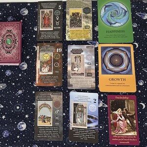May include: A tarot card spread with ten cards laid out on a dark blue fabric with a white star pattern. The cards are from the "The Wild Unknown" tarot deck. The cards are: The Empress, 5 of Pentacles, The Chariot, 19 The Sun, Clarity, Growth,  The World, 2 of Pentacles, and True Love Feelings.