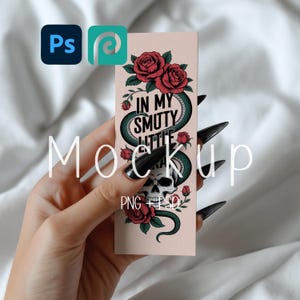 Puede incluir: Un marcapáginas rectangular con un diseño de calavera, serpiente y rosas. Se muestra el texto "IN MY SMUTY LITTLE GRAVE". El marcapáginas se sostiene en una mano con uñas largas y negras. La palabra "Mockup" está escrita en la imagen.