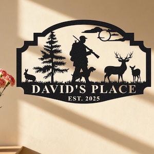 Può includere: Cartello in metallo nero con la silhouette di un cacciatore con fucile, cane, cervi e conigli. Il cartello recita "DAVID'S PLACE EST. 2025" in una cornice decorativa, adatta all'esposizione.