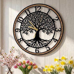 May include: A round wall clock featuring a black metal cutout of a tree with roots in the center. The clock has a light wood-toned outer frame, black Arabic numerals from one to twelve, and two gold-colored hands indicating the time.