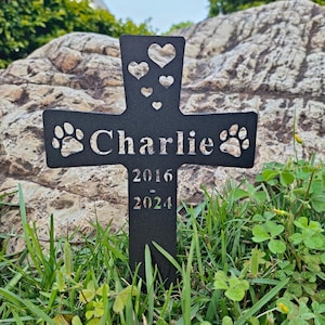 May include: Black metal cross with paw prints and hearts, personalized with the name "Charlie" and the dates "2016 - 2024".