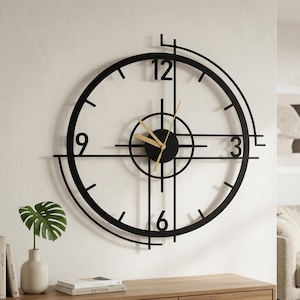 Puede incluir: Un gran reloj de pared circular con un marco de metal negro, líneas geométricas y un diseño de cruz central. La esfera muestra los números 3, 6, 9 y 12 en una fuente negra, complementada con manecillas finas de color dorado para la hora.
