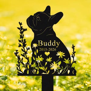May include: Black metal garden stake featuring a silhouette of a French Bulldog. The stake includes the name "Buddy" with the years 2015-2026, a heart, and floral accents. The background is a field of yellow flowers.