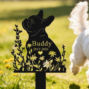 May include: Black metal garden stake featuring a silhouette of a French Bulldog with the name "Buddy" and dates 2015-2026. The dog is surrounded by floral and plant cutouts. A white dog is in the background.