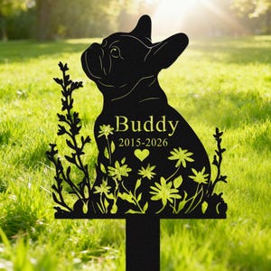 May include: Black metal garden stake featuring a silhouette of a French Bulldog. The stake includes the name "Buddy", dates 2015-2026, and floral accents. The stake is designed to be placed in a garden or yard.