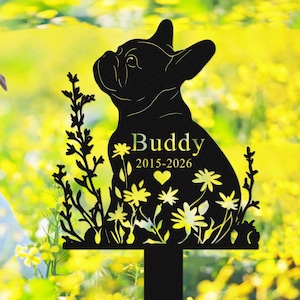 May include: Black metal garden stake featuring a silhouette of a French Bulldog. The stake includes the name "Buddy" and the years "2015-2026", along with floral and heart details. The background is a blurred yellow.