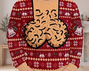 May include: A red long-sleeve knit sweater featuring a repeating pattern of white snowflakes and bells with holly. The center of the chest displays a large, tan, textured graphic design with black outlines, set against a tan rectangular background.