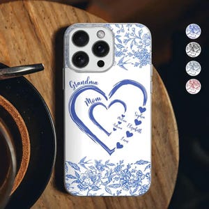 May include: A white phone case with a blue floral design and a heart-shaped graphic. The graphic includes the words "Grandma" and "Mom", with names inside the heart. The case has a clear border.