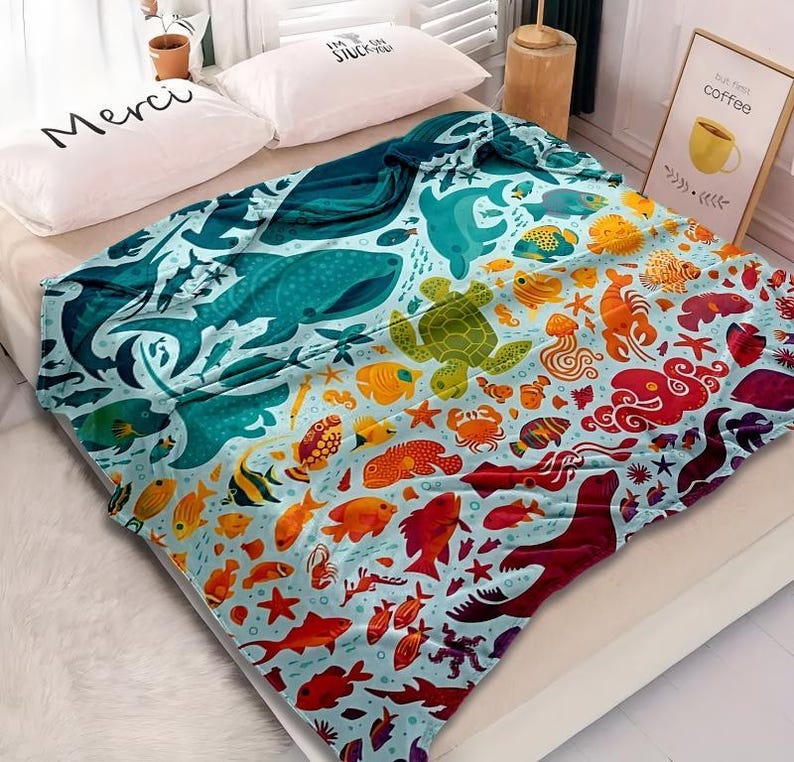 May include: A colorful blanket featuring an ocean-themed design. The blanket showcases various marine life, including whales, turtles, and fish, in shades of blue, green, orange, and red. The blanket is made of soft material and is suitable for a bed or couch.