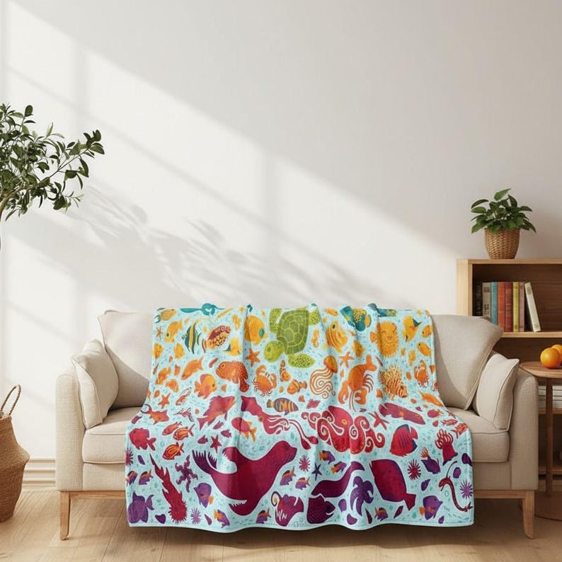 May include: A colorful blanket featuring a vibrant array of sea creatures, including fish, turtles, and octopuses. The design transitions from blue to red, creating a gradient effect. The blanket is draped over a beige sofa.