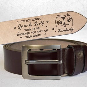 May include: A brown leather belt with a silver buckle. The belt's tip is engraved with the text "IT'S NOT GONNA SPANK ITSELF THINK OF ME WHENEVER YOU TAKE OFF YOUR PANTS" and a graphic of a rear end with handprints. The name "Kimberly" is also engraved.