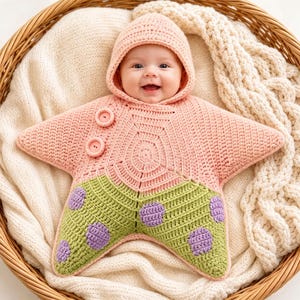 May include: A crochet baby bunting in the shape of a five-pointed star. The garment is light pink with a hood, featuring two light pink buttons on the upper right side. The lower portion is light green with purple circular spots throughout.