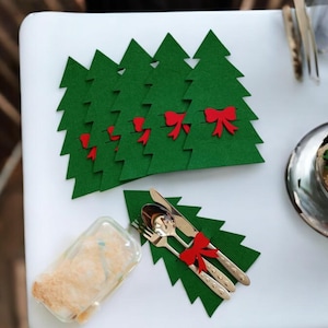 May include: Set of green felt Christmas tree place card holders with red bows. Each holder is designed to hold a single utensil, such as a fork or knife.