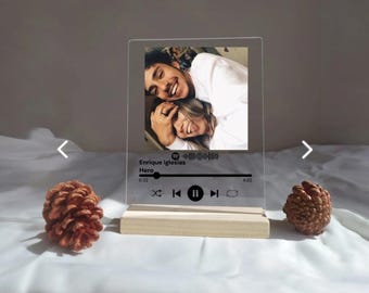 May include: A clear acrylic photo frame with a wooden base. The frame features a photo of a couple and a Spotify music player design with the song "Hero" by Enrique Iglesias. The music player shows the song title, artist, and a progress bar.