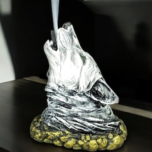 May include: A white ceramic incense burner shaped like a wolf howling at the moon. The wolf is detailed with textured fur and a gold base.