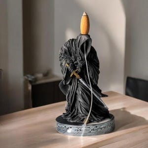 May include: Black incense burner shaped like a hooded figure holding a sword. The figure is standing on a round base with the inscription "One Ring to rule them all" in Elvish script.