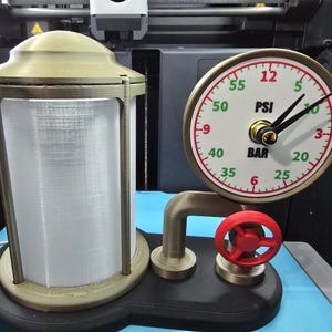 May include: A unique steampunk-style clock with a pressure gauge face, displaying PSI and BAR measurements. The clock has a brass-colored frame and a red valve wheel. A cylindrical, brass-colored structure sits beside the clock.