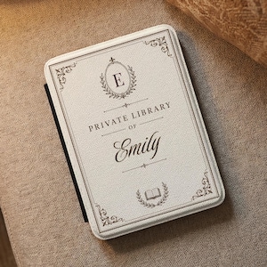 May include: A rectangular e-reader case with a textured off-white fabric finish. The cover features a dark brown decorative border, a central oval laurel wreath with the letter E, and the text PRIVATE LIBRARY OF Emily in dark brown ink.