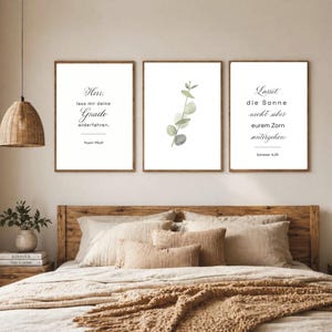 Könnte beinhalten: Drei gerahmte Wandkunstdrucke mit inspirierenden Zitaten und botanischen Illustrationen. Die Drucke befinden sich in Holzrahmen und hängen über einem Bett mit neutralfarbener Bettwäsche. Der Text auf den Drucken ist auf Deutsch.