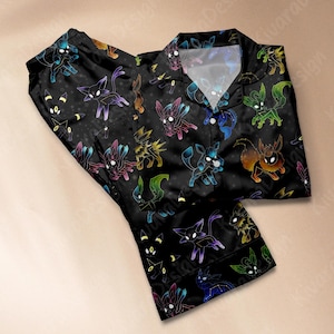 Op de afbeelding: Zwarte pyjamaset met een herhaald patroon van kleurrijke, gestileerde wezens en sterren. De top heeft een knoopontwerp met een kraag en de broek heeft een elastische tailleband. De wezens zijn omlijnd in verschillende kleuren, waaronder blauw, groen en geel.