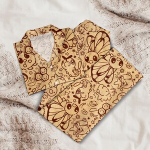 K&ouml;nnte beinhalten: Beige Pyjama-Set mit einem braunen Cartoon-Charakter-Muster. Das Set beinhaltet ein Hemd mit Kn&ouml;pfen und eine passende Hose. Der Stoff hat ein weiches, strukturiertes Aussehen. Das Design zeigt verschiedene Cartoon-Charaktere, Blumen und geometrische Formen.