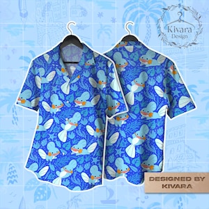 Puede incluir: Camisa azul con botones con un patrón repetido de criaturas acuáticas de dibujos animados, aletas blancas y plantas marinas. La camisa se muestra en una percha negra. Diseño de Kivara.