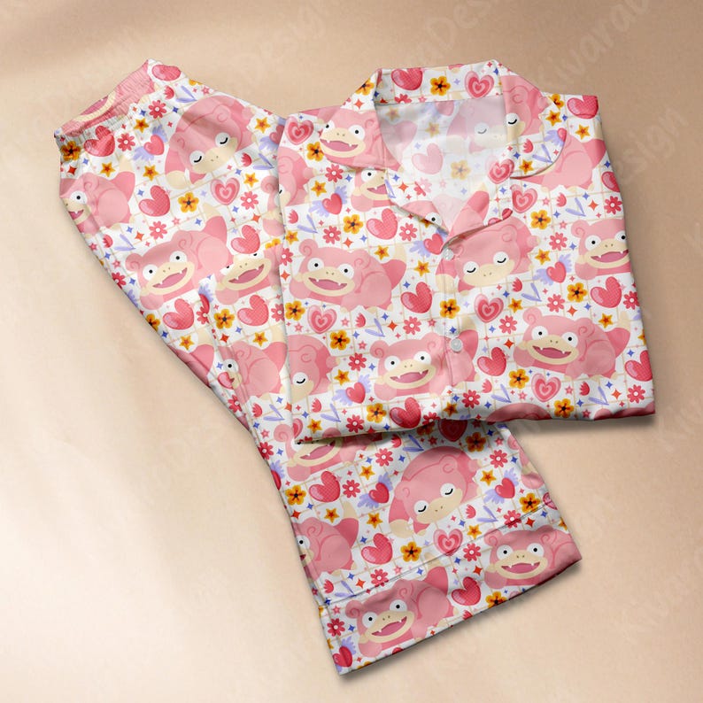 K&ouml;nnte beinhalten: Rosa Pyjama-Set mit einem sich wiederholenden Muster aus Zeichentrickfiguren, Herzen und Blumen auf wei&szlig;em Hintergrund. Das lang&auml;rmlige Oberteil hat einen Kragen und einen Knopfverschluss. Die Pyjamahose hat einen elastischen Bund.