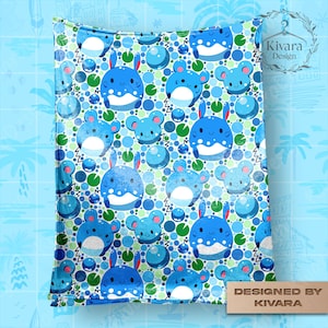 May include: A rectangular blanket featuring a repeating pattern of blue cartoon creatures with rabbit-like ears, round blue spheres, and small green lily pads on a white background. The design includes the text Kivara Design in the top right corner.