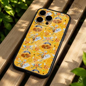 Pode incluir: Uma capa de telefone preta com um padrão repetido de abelhas, favos de mel e colmeias em um fundo amarelo. A capa tem um acabamento brilhante e uma borda preta. O design inclui o texto "Kivara Design".