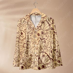 K&ouml;nnte beinhalten: Ein lang&auml;rmliges Button-Down-Hemd mit beigem Hintergrund und einem sich wiederholenden braunen Cartoon-Muster verschiedener Kreaturen, Schmetterlinge und Blumen. Das Hemd h&auml;ngt an einem Holzb&uuml;gel.