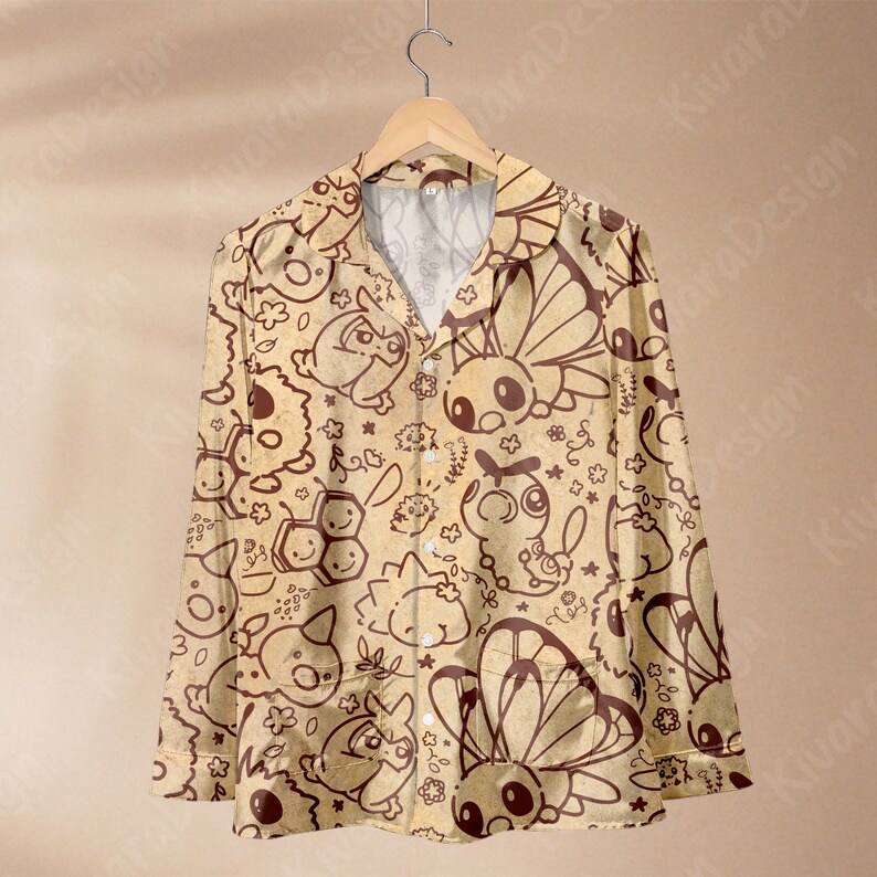 K&ouml;nnte beinhalten: Ein lang&auml;rmliges Button-Down-Hemd mit beigem Hintergrund und einem sich wiederholenden braunen Cartoon-Muster verschiedener Kreaturen, Schmetterlinge und Blumen. Das Hemd h&auml;ngt an einem Holzb&uuml;gel.