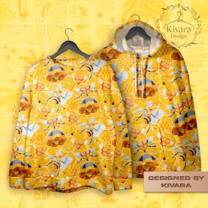 May include: A yellow sweatshirt and hoodie with a repeating pattern of bees, honeycombs, and geometric shapes. The hoodie has a drawstring and a white interior. The sweatshirt is long-sleeved. The design is "Designed by KIVARA."