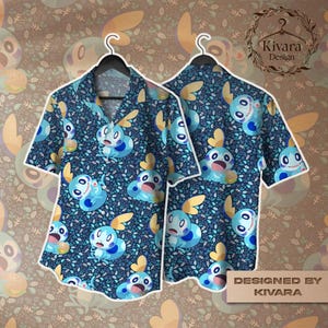 May include: A short-sleeved button-down shirt with a blue background and a repeating pattern of blue and yellow cartoon characters. The shirt is displayed on a black hanger. The design includes the text "Designed by KIVARA".